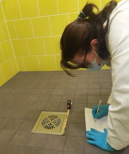 A student is on the shower floor measuring the floor drain.
