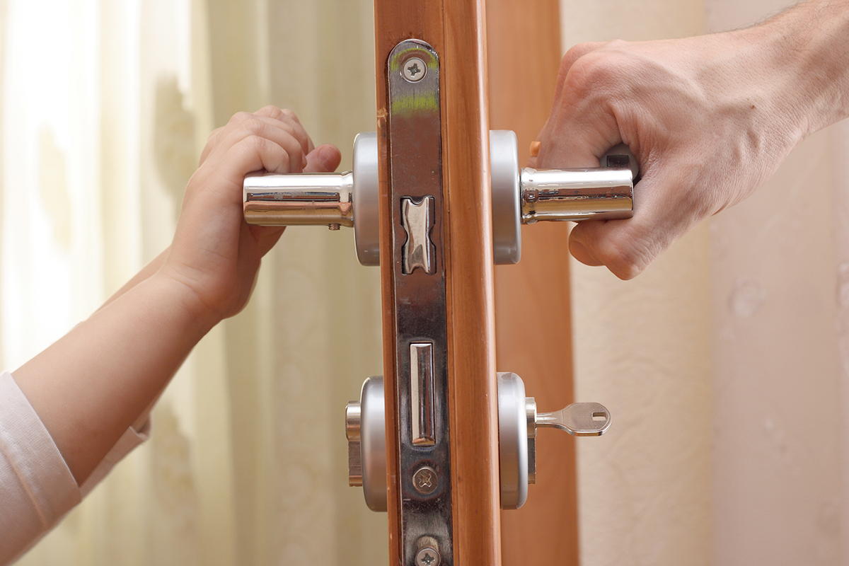 Door handle, a child's hand on the other side and an adult's hand on the other.