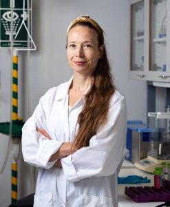 A woman poses in a laboratory wearing a white coat.