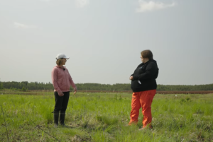 Kuvakaappaus videosta, jossa kaksi naista seisoo vihreällä pellolla.