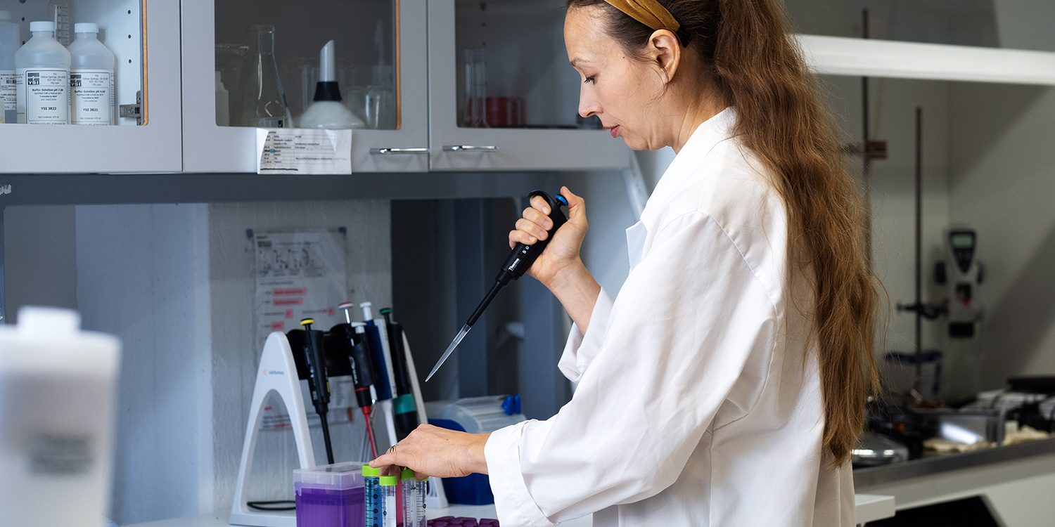 Naishenkilö pipetoi laboratoriossa valkoinen takki päällä.