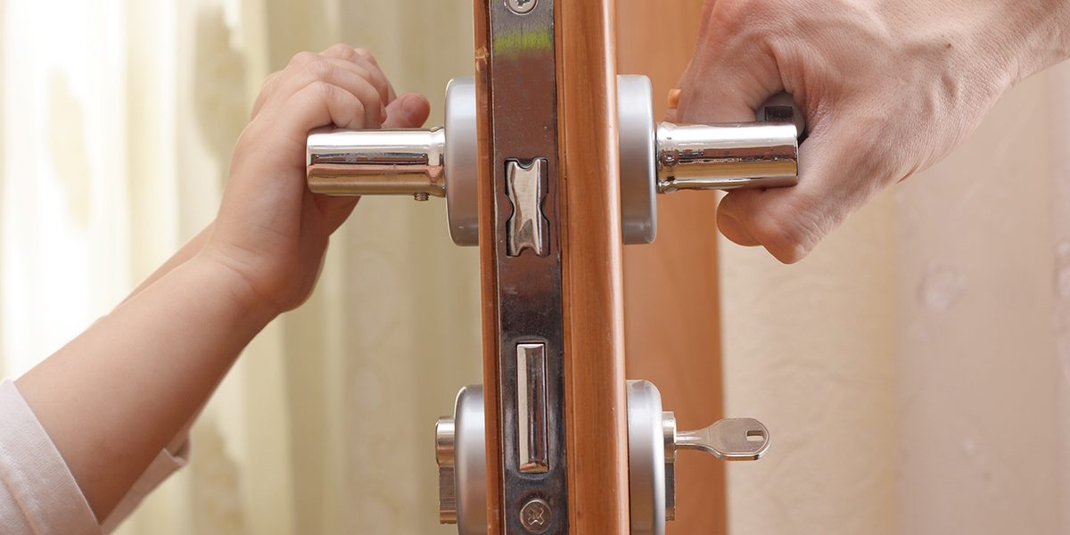 Door handle, a child's hand on the other side and an adult's hand on the other.